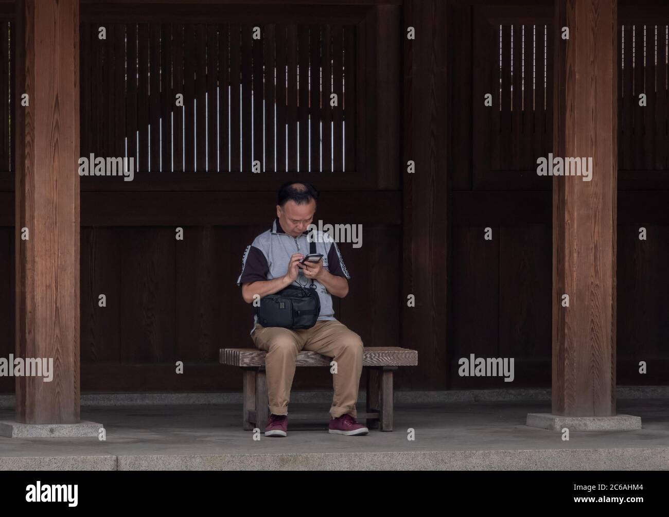 Anziano giapponese seduto su una panchina di legno con smartphone in Meiji Jingu interno composto, Tokyo, Giappone Foto Stock