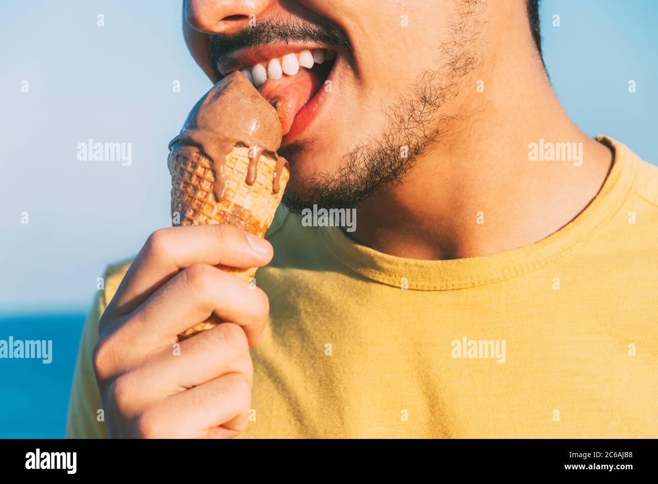 il giovane in giallo lecca il gelato al cioccolato Foto Stock