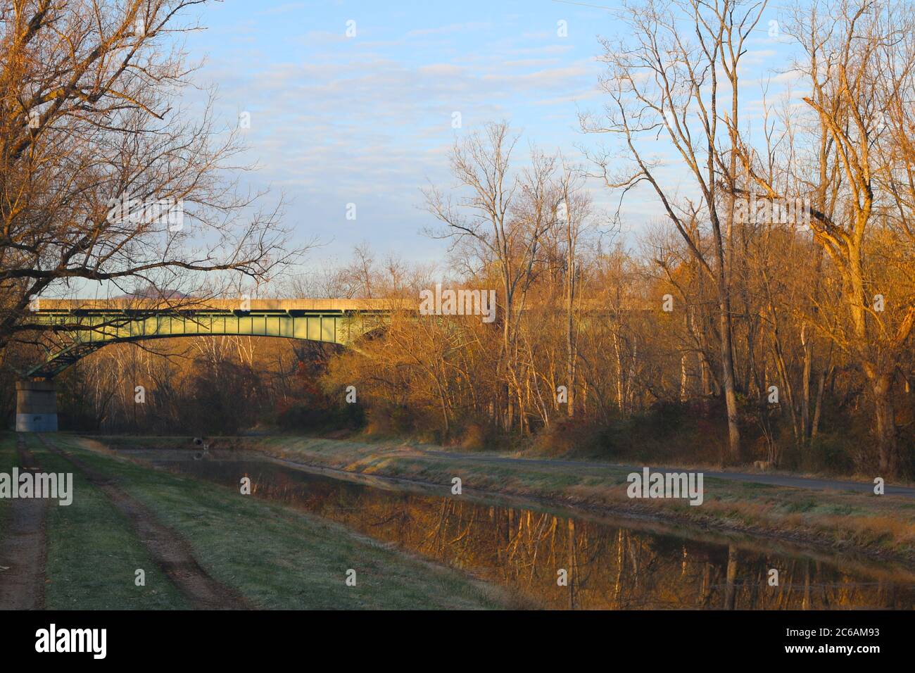 un alto ponte in acciaio su un canale rurale con riflesso dell'alba e della foresta Foto Stock