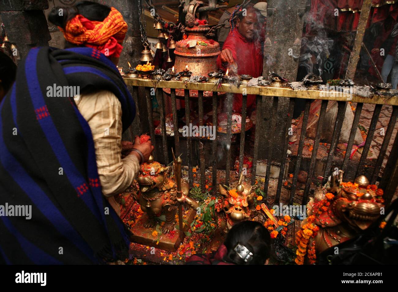 Sommo sacerdote raffigurato accanto al grande ghanta (campana rituale indù) e lampade ad olio rituale nel santuario principale nel tempio di Dakshinkali vicino a Kathmandu, Nepal. Uno dei templi indù più importanti del Nepal dedicato alla dea Kali è noto per i suoi sacrifici animali che si svolgono nel santuario principale. Foto Stock