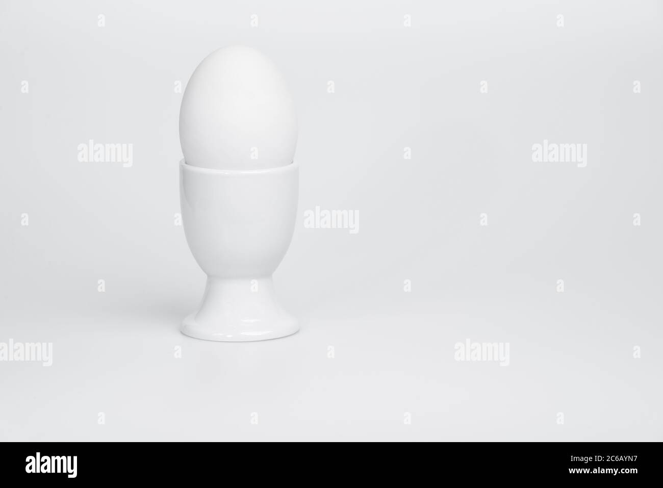 Una vista leggermente rialzata di un uovo d'anatra bianco in una tazza d'uovo bianca su uno sfondo bianco. Foto Stock