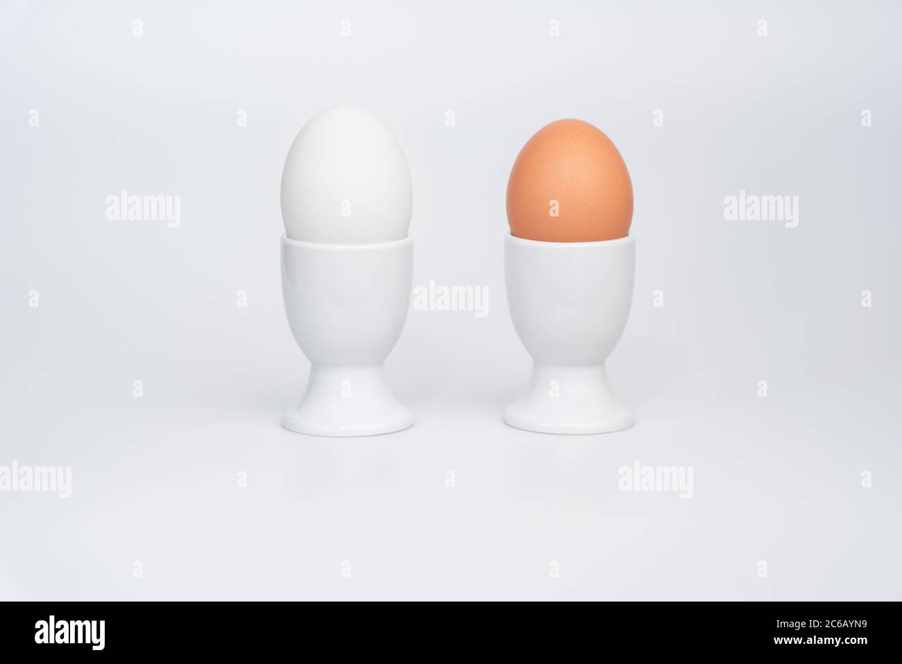 Un uovo d'anatra bianco e un uovo di pollo marrone in coppette bianche su sfondo bianco Foto Stock