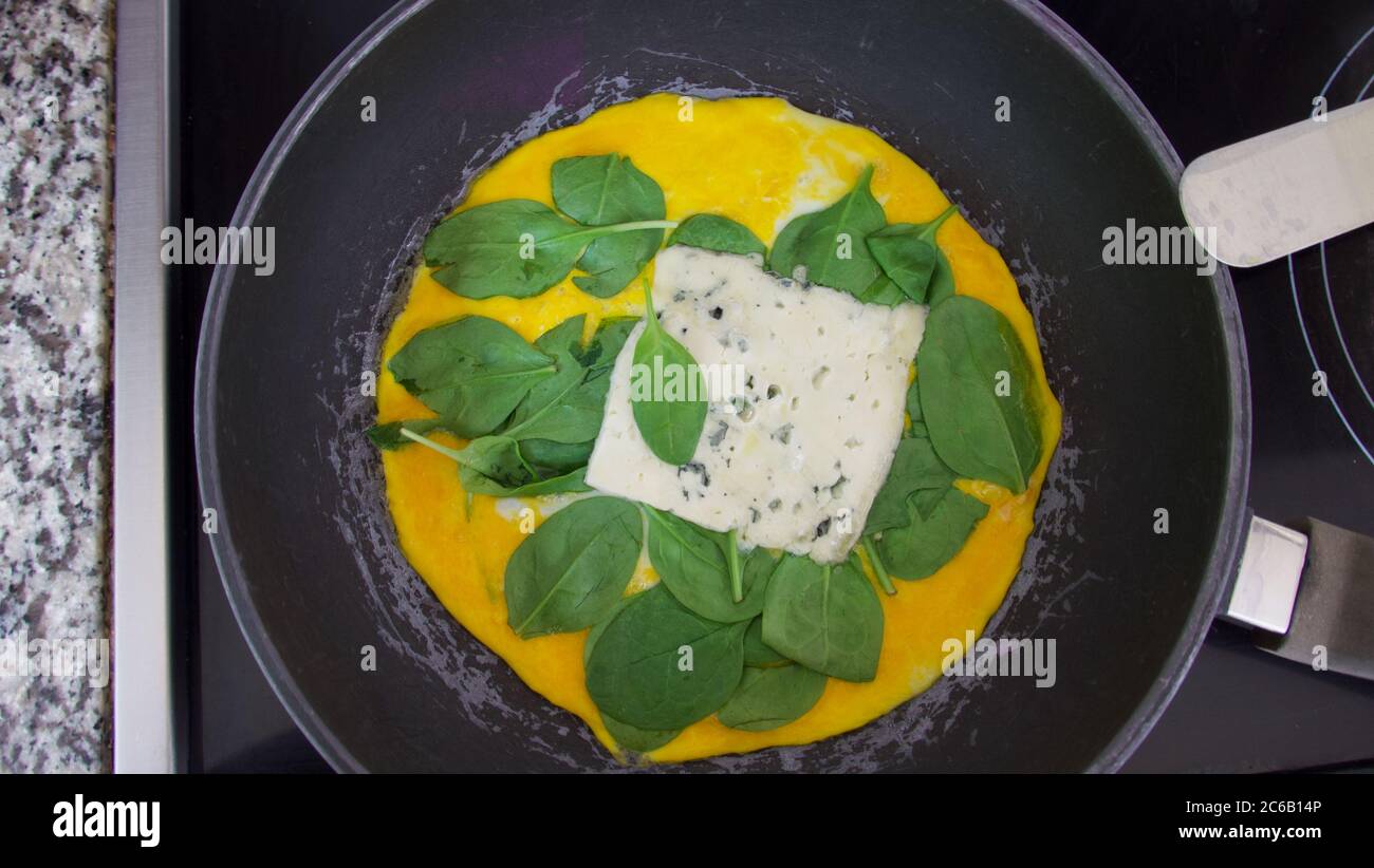 Cottura di frittate con spinaci e omelette di formaggio in padella sul piano cottura Foto Stock