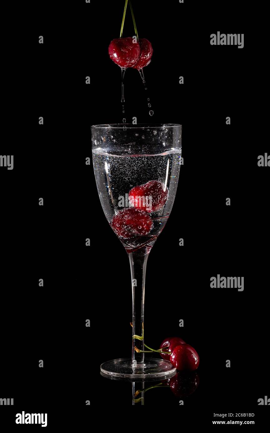 Foto flash ad alta velocità con ciliegie che spruzzano nel bicchiere da vino Foto Stock