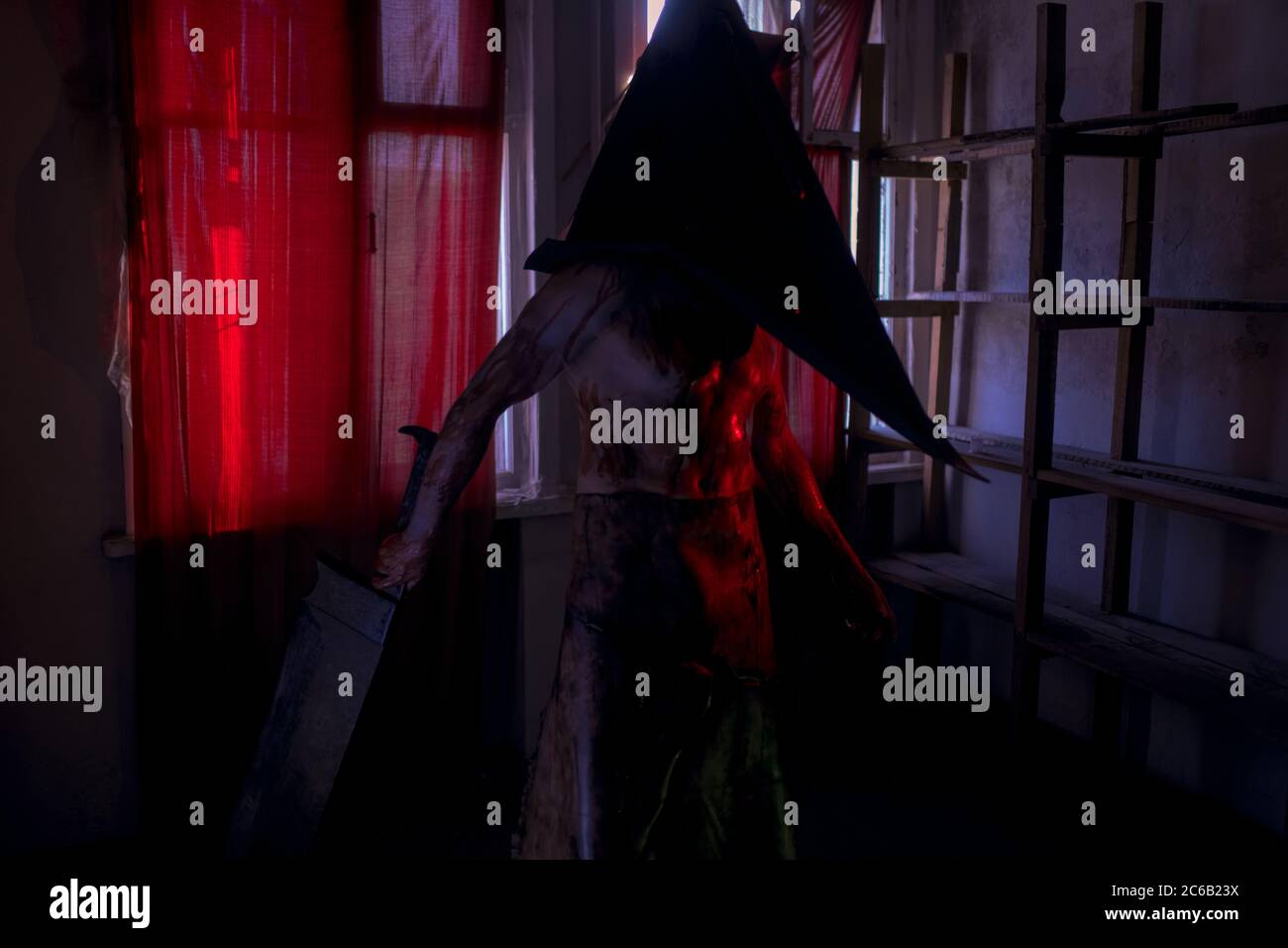 Cosplayer a immagine di carnefice si trova in camera oscura con coltello in mano e casco sulla testa. Foto Stock