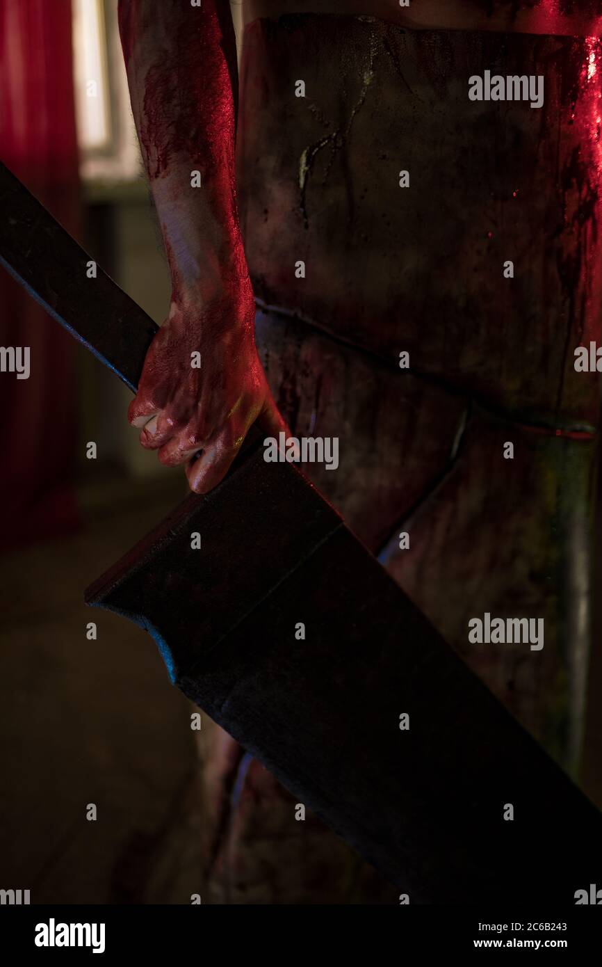 Cosplayer a immagine di carnefice si trova in una stanza buia in grembiule con coltello in mano. Primo piano. Foto Stock