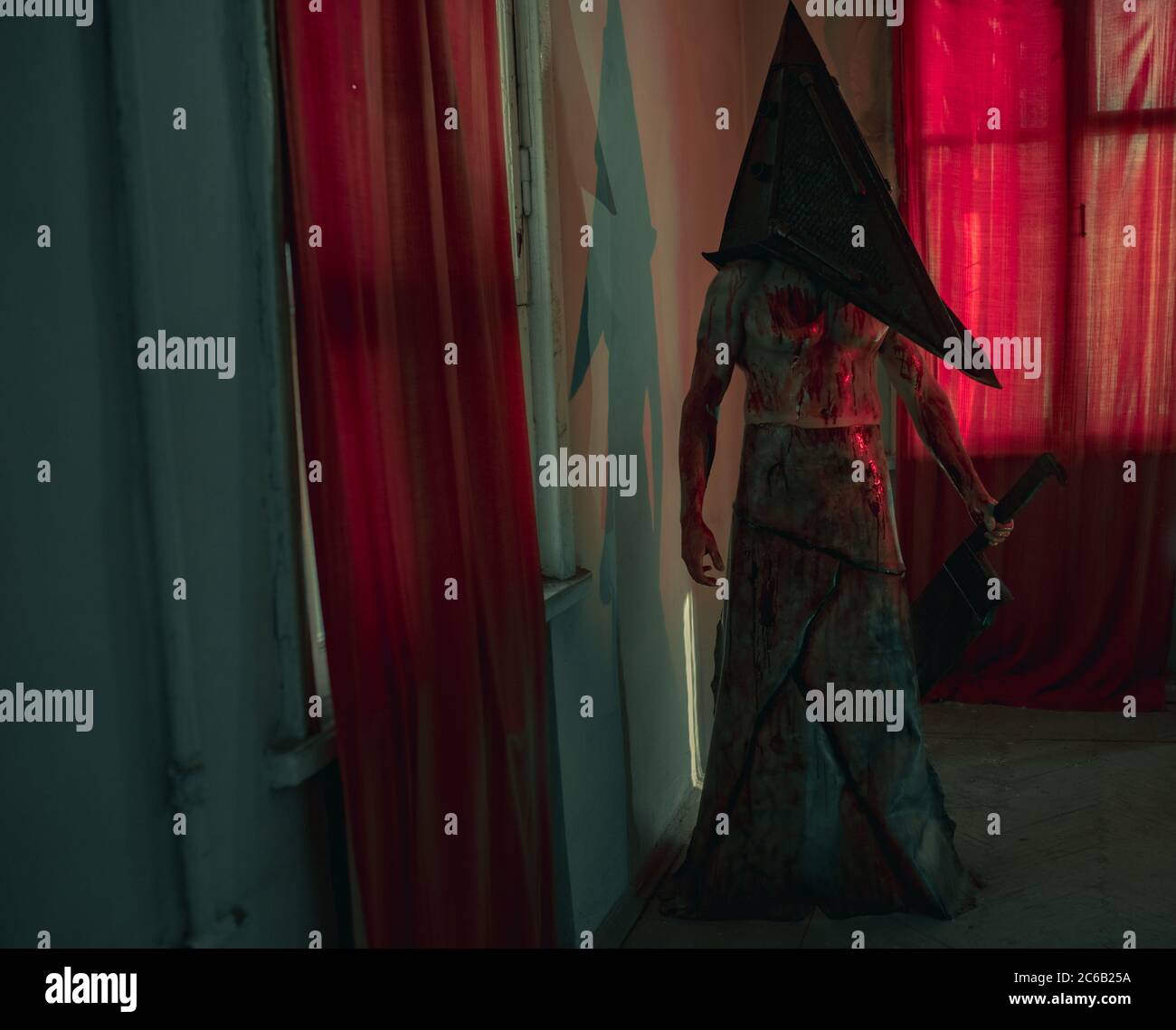 Cosplayer a immagine di carnefice si trova in camera oscura con coltello in mano e casco sulla testa. Foto Stock