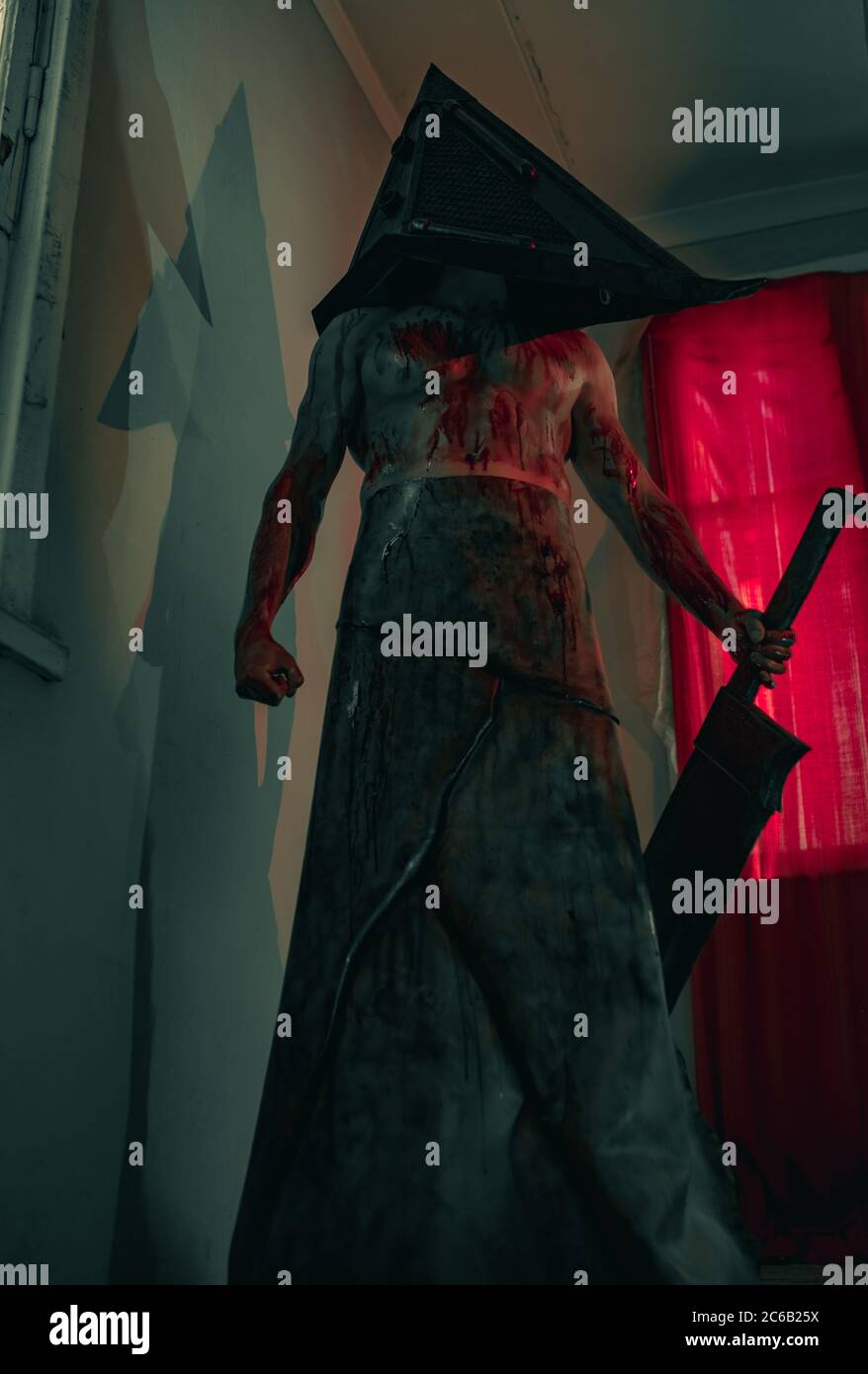 Cosplayer a immagine di carnefice si trova in camera oscura con coltello in mano e casco sulla testa. Foto Stock