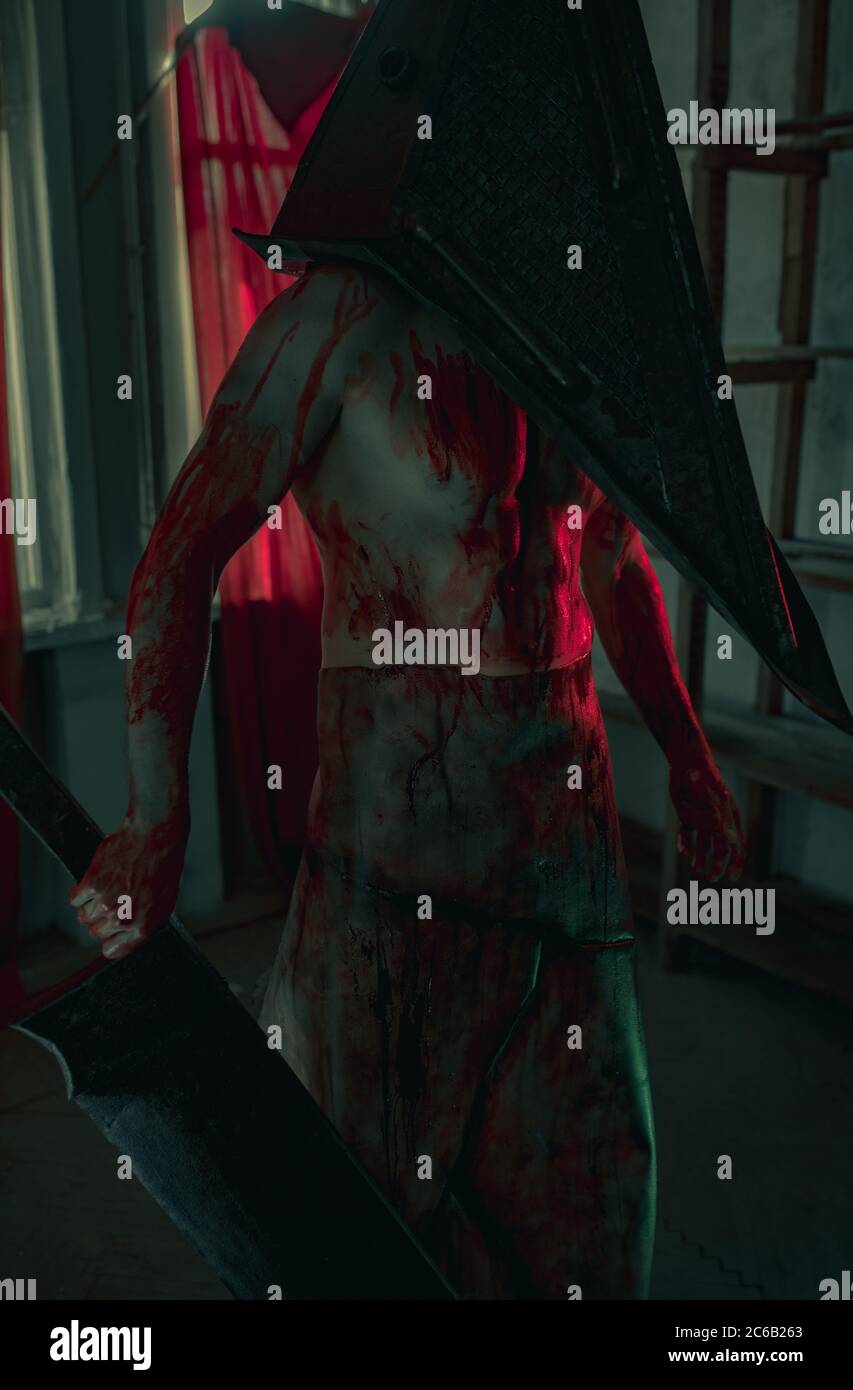 Cosplayer a immagine di carnefice si trova in camera oscura con coltello in mano e casco sulla testa. Foto Stock