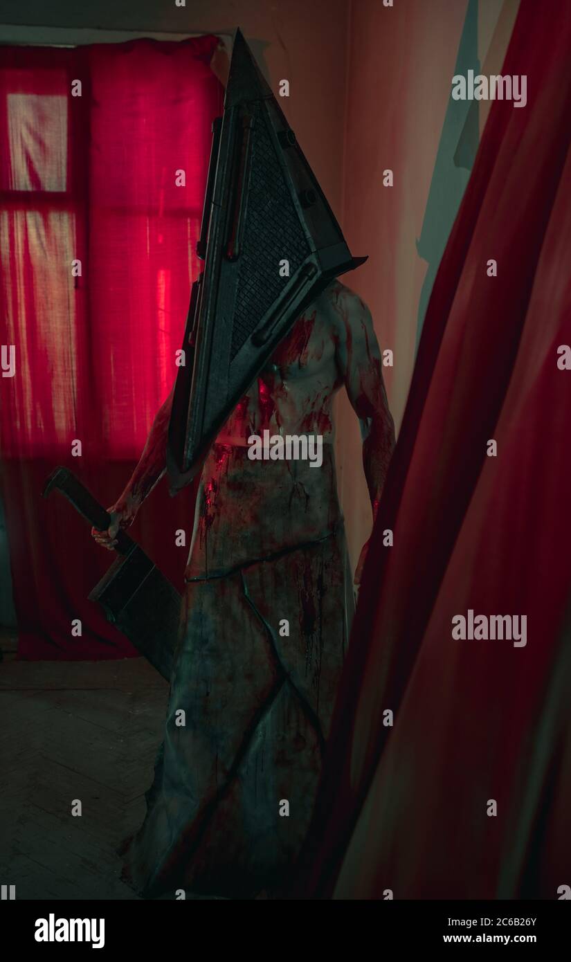 Cosplayer a immagine di carnefice si trova in camera oscura con coltello in mano e casco sulla testa. Foto Stock