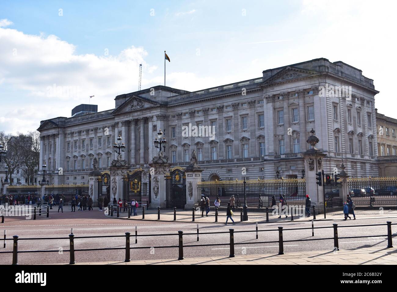 Alcuni turisti e visitatori camminano oltre le ornate ringhiere nere e dorate di Buckingham Palace. La bandiera è stata fatta volare a pieno albero sopra il palazzo. Foto Stock