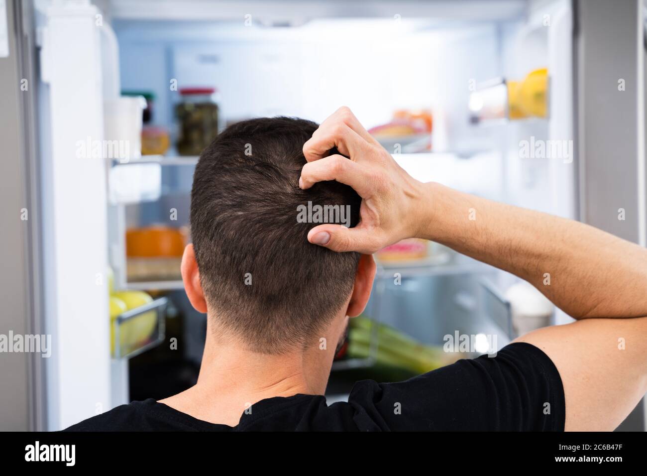 Affamato uomo confuso guardando in Open Frigo in cucina Foto Stock