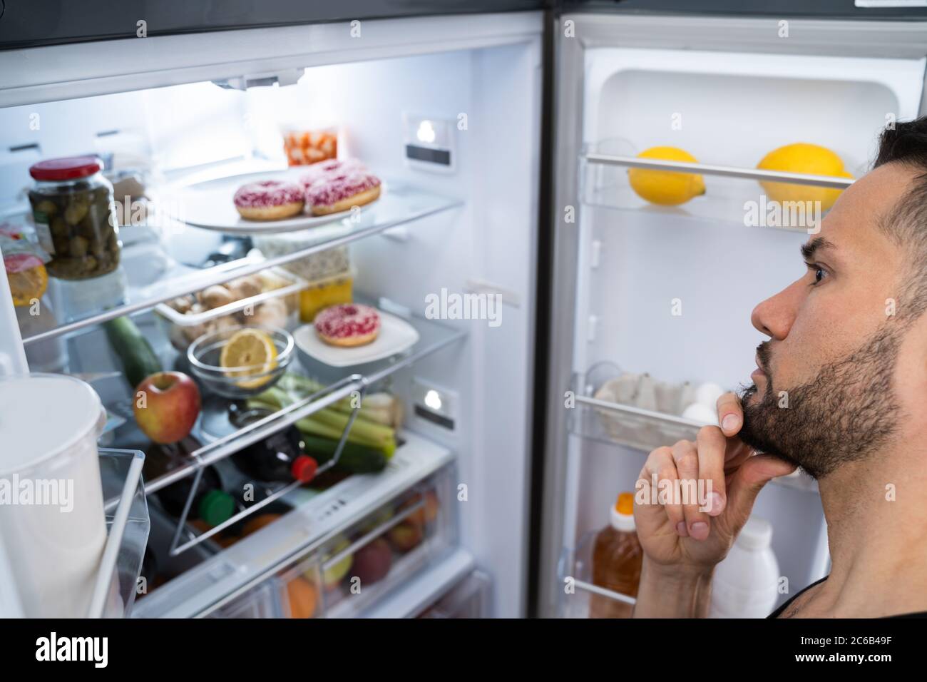 Affamato uomo confuso guardando in Open Frigo in cucina Foto Stock