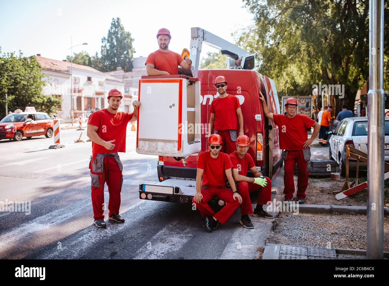 Sei operai caucasici in tute da lavoro rosse si trovano accanto a un  furgone gru sul cantiere. Impostazione dei semafori sulla strada Foto stock  - Alamy