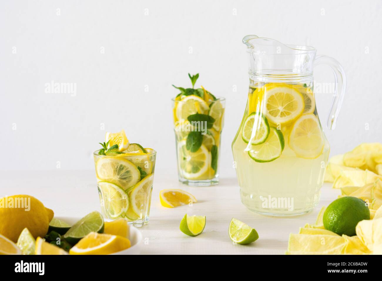 Bevanda estiva rinfrescante di limone, lime e menta, caraffa con limonata e bicchieri e fette di agrumi Foto Stock