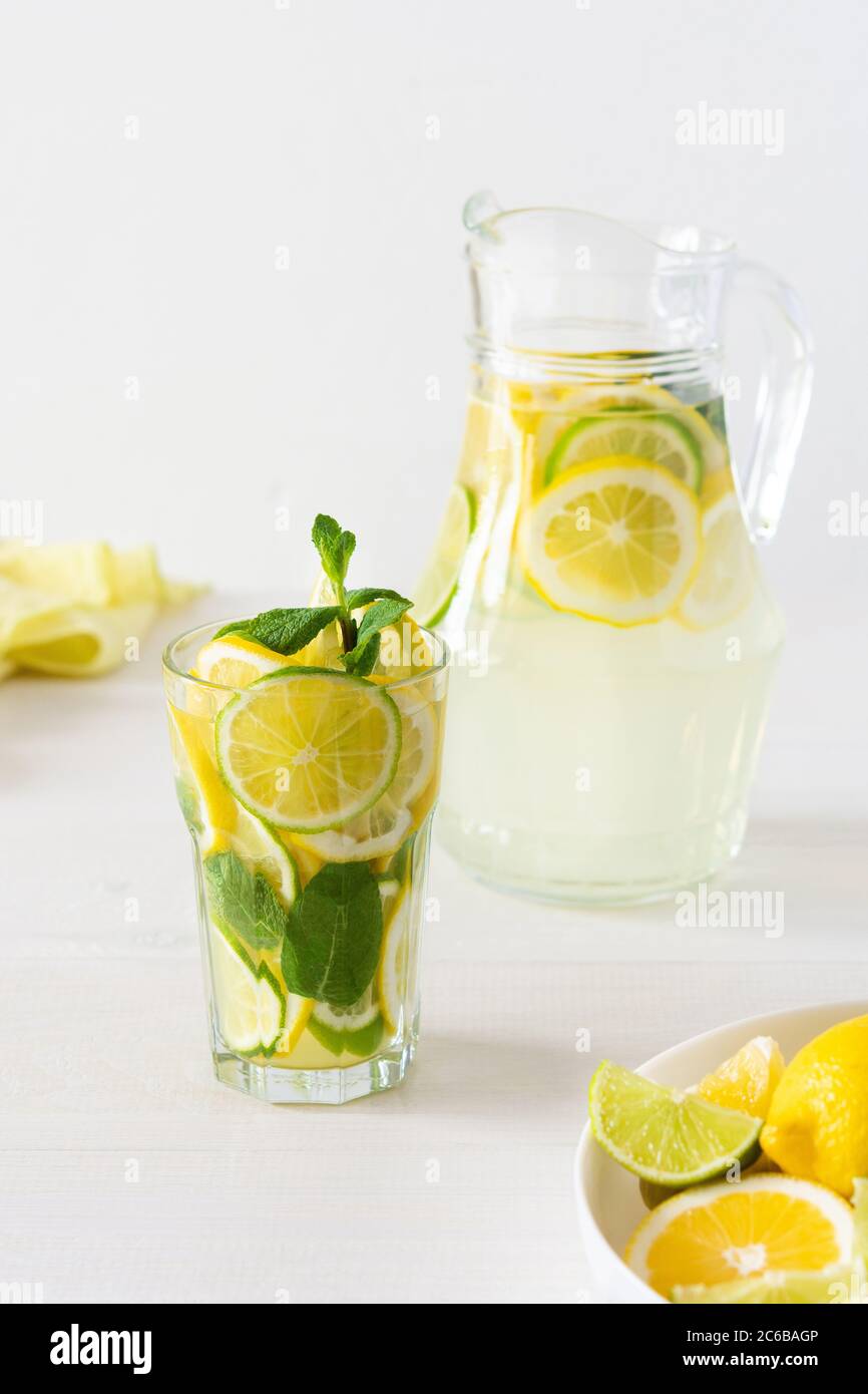 Bevanda estiva rinfrescante di limone, lime e menta, caraffa con limonata e bicchieri e fette di agrumi Foto Stock