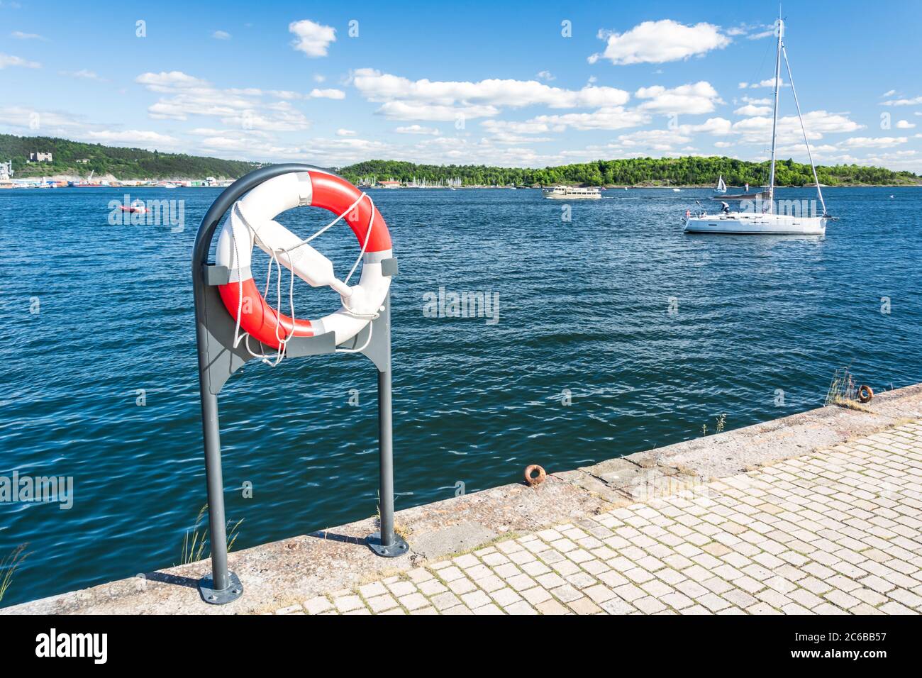 Salvagente sul lungomare in estate con barche a vela sullo sfondo Foto Stock