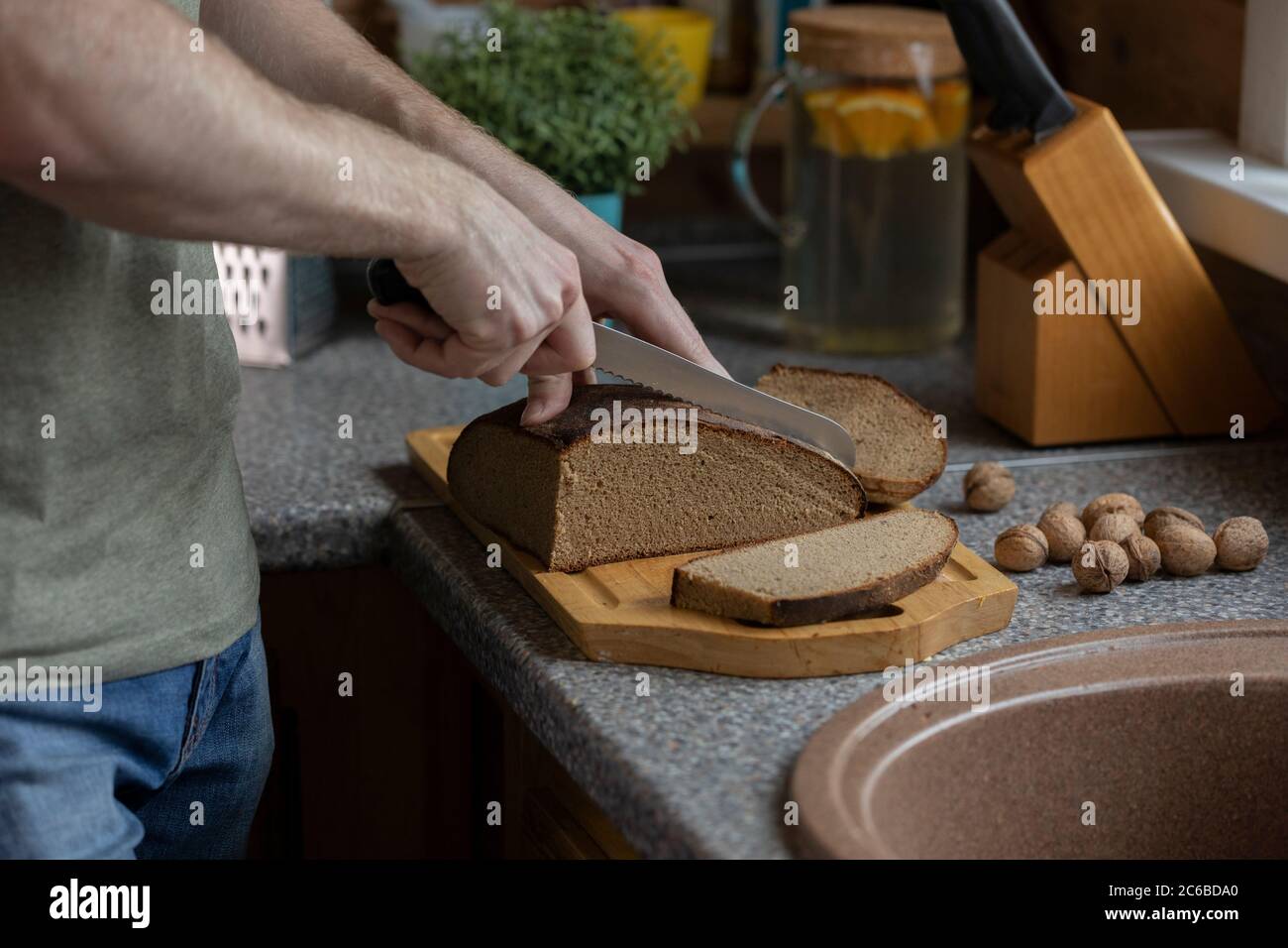 Mano dell'uomo che taglia il pane di segale su tavola di legno con coltello  su cucina rustica Foto stock - Alamy