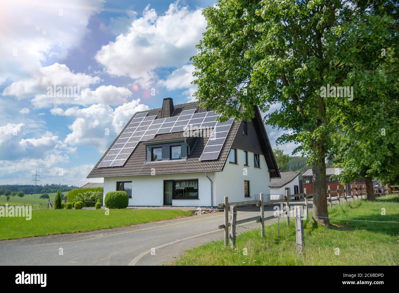 Una casa con pannelli solari sul tetto. Una fattoria è alimentata da energia solare. Sullo sfondo sono stalle. Casa in natura verde. Cielo blu con nuvole Foto Stock