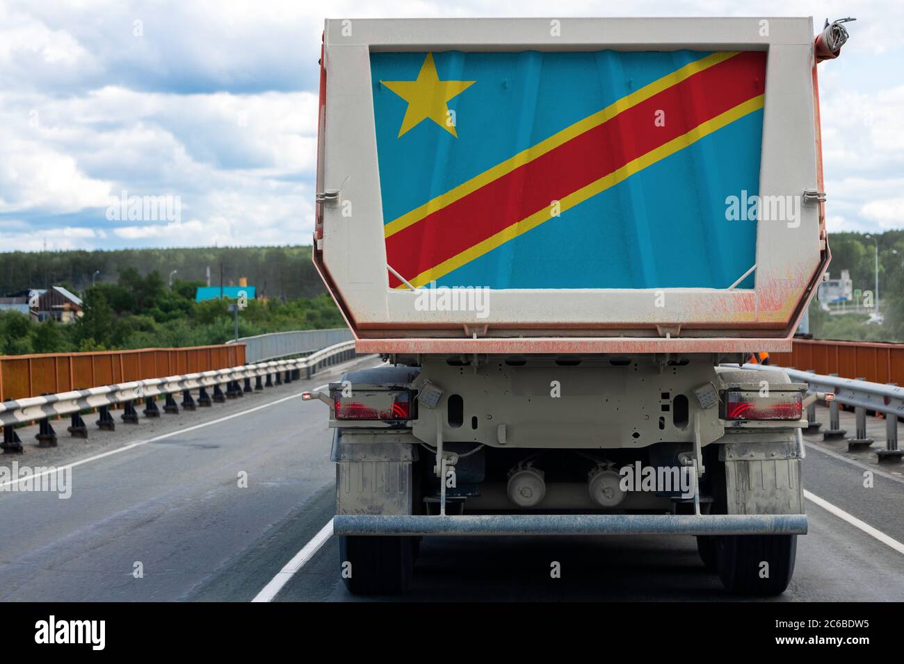 Grande camion con la bandiera nazionale della Repubblica Democratica del Congo che si muove sulla strada, sullo sfondo del villaggio e paesaggisti foresta Foto Stock