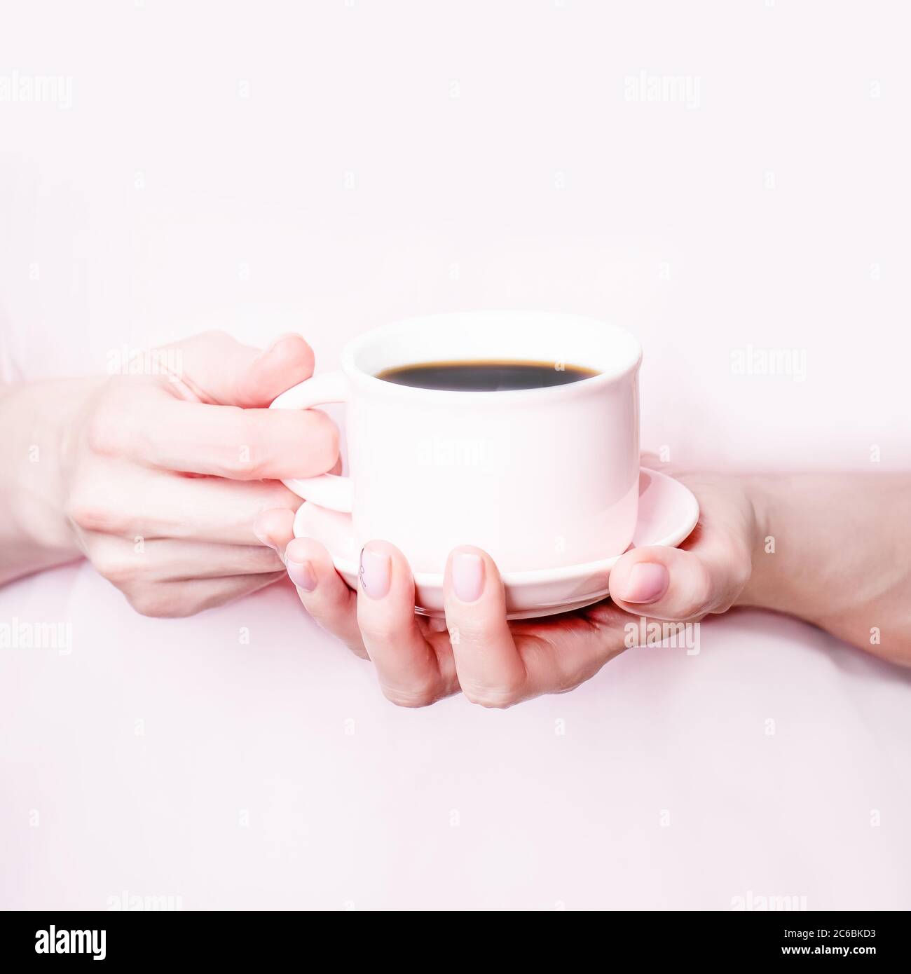 Mani femminili che tengono una tazza rosa di caffè nero su sfondo rosa. Spazio di copia Foto Stock