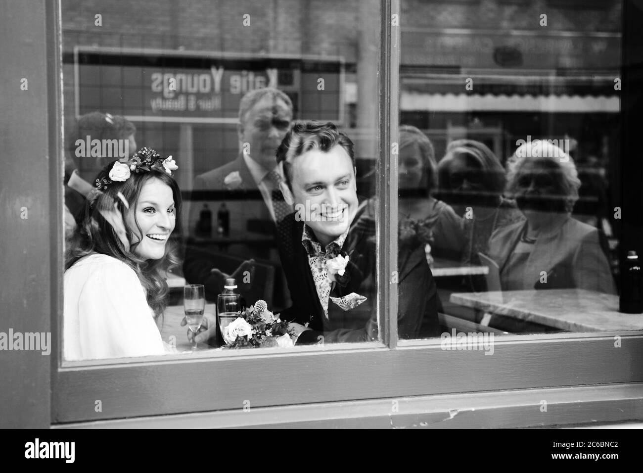 Coppia sorridente, uomo e donna, anni '20 / '30, cena al ristorante cafe che guarda fuori finestra per la famiglia e gli amici che si riflettono nelle finestre. Foto Stock