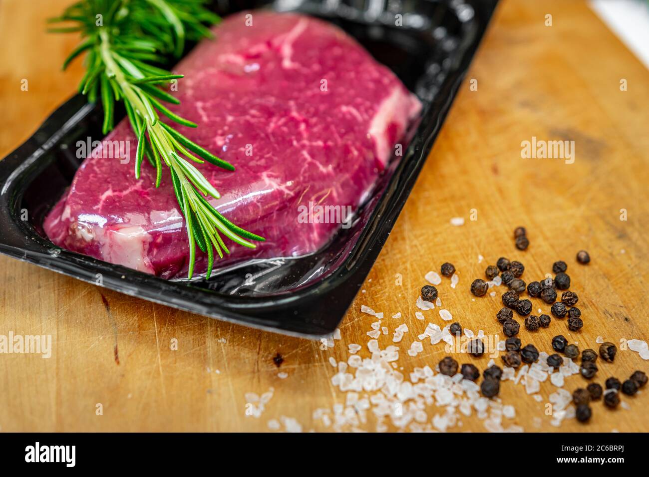 Bistecca di manzo in confezionamento sottovuoto e spezie su tagliere di legno Foto Stock