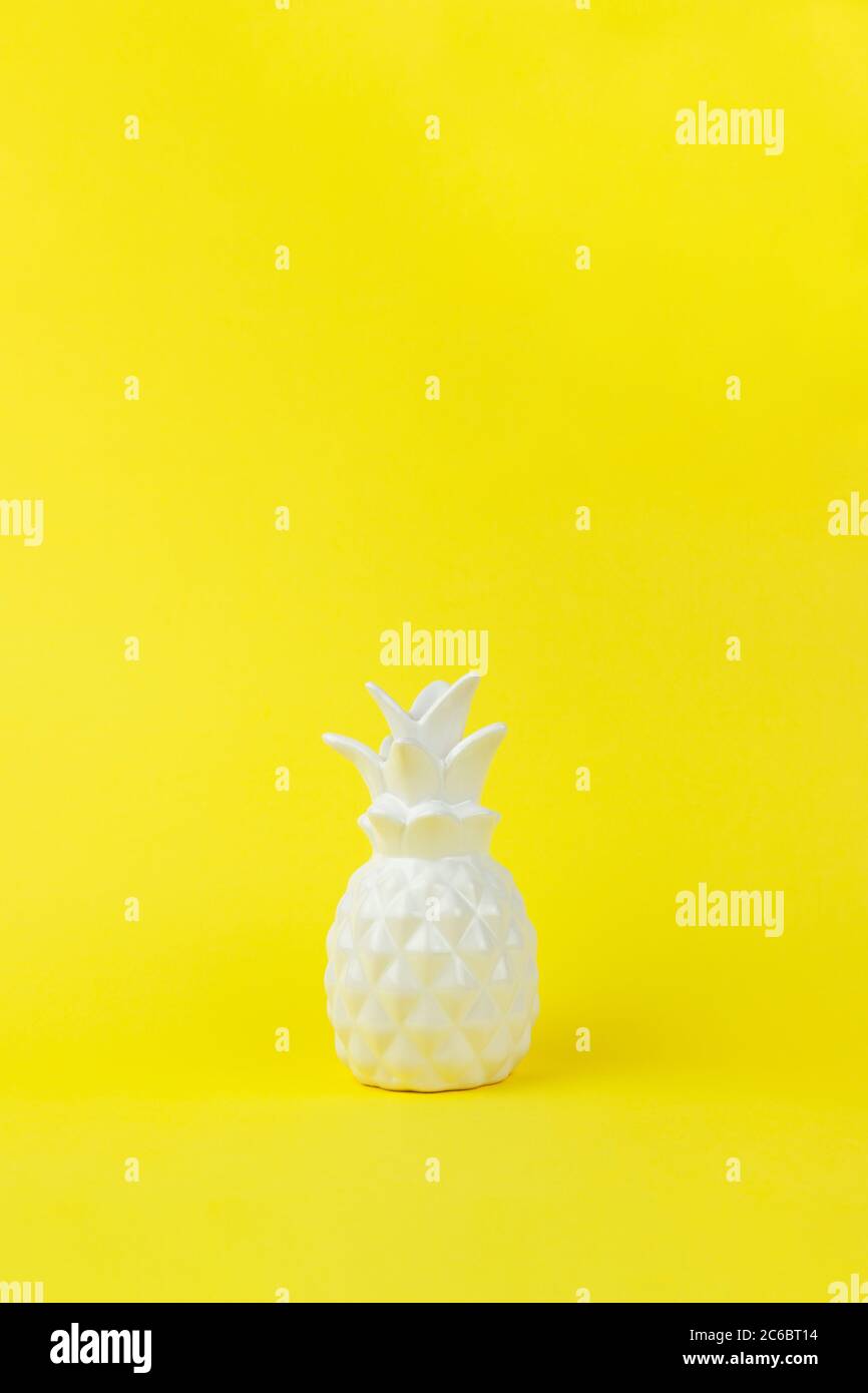 Pezzo trendy di interno bianco ananas ceramico lucido su sfondo di carta giallo, spazio copia. Stile minimalista del decor. Verticale. Per lo stile di vita Foto Stock