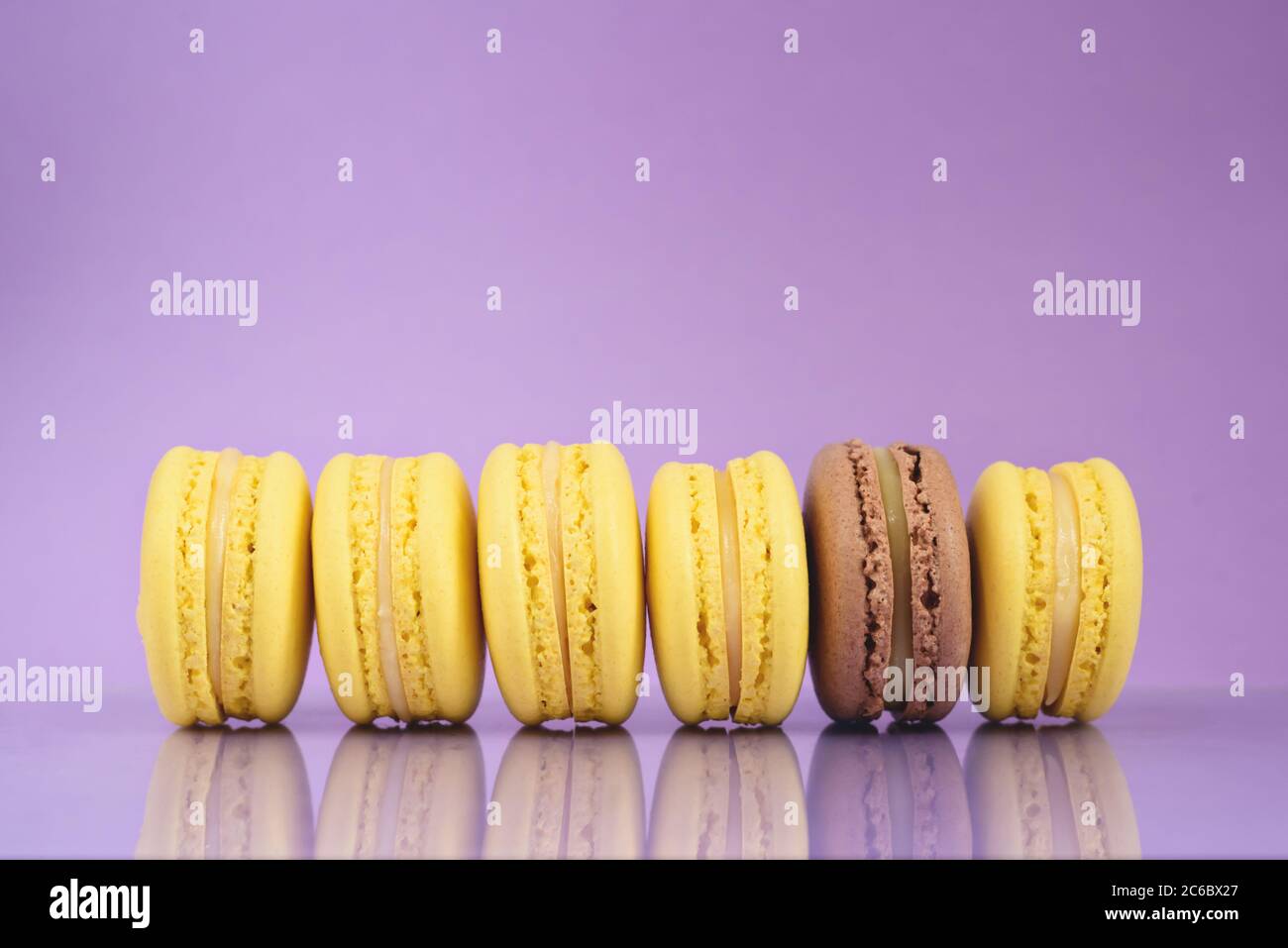 Fila di macaron colorati perfetti su sfondo viola. Vista frontale. Foto Stock