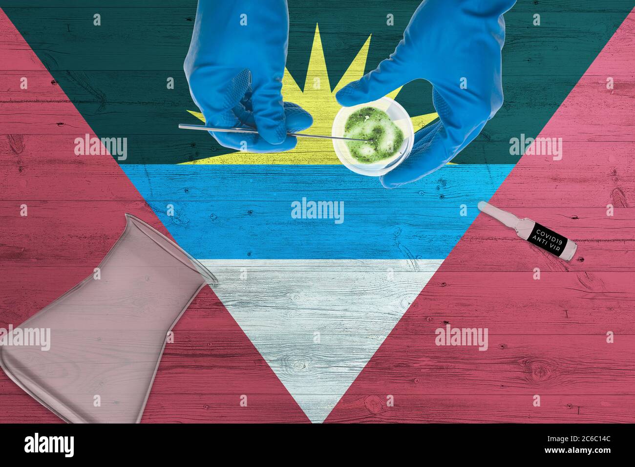 Antigua e Barbuda bandiere sul tavolo da laboratorio. Medico tecnico sanitario che tiene il kit di raccolta con tampone COVID-19, indossando guanti protettivi blu, ep Foto Stock