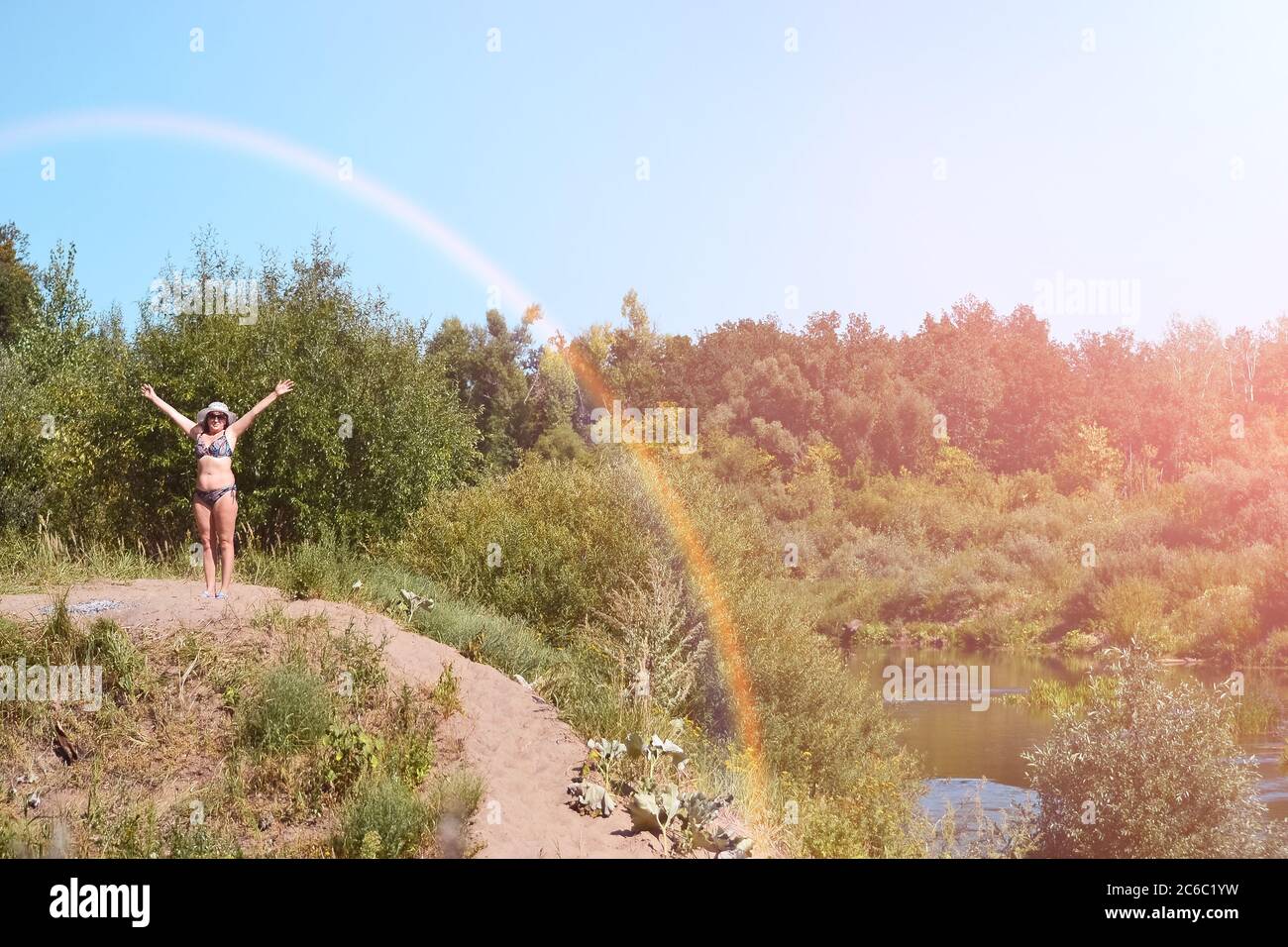Una donna con occhiali scuri su una collina in lontananza si alza con le mani sollevate al cielo blu. Concetti di libertà di circolazione in natura Foto Stock