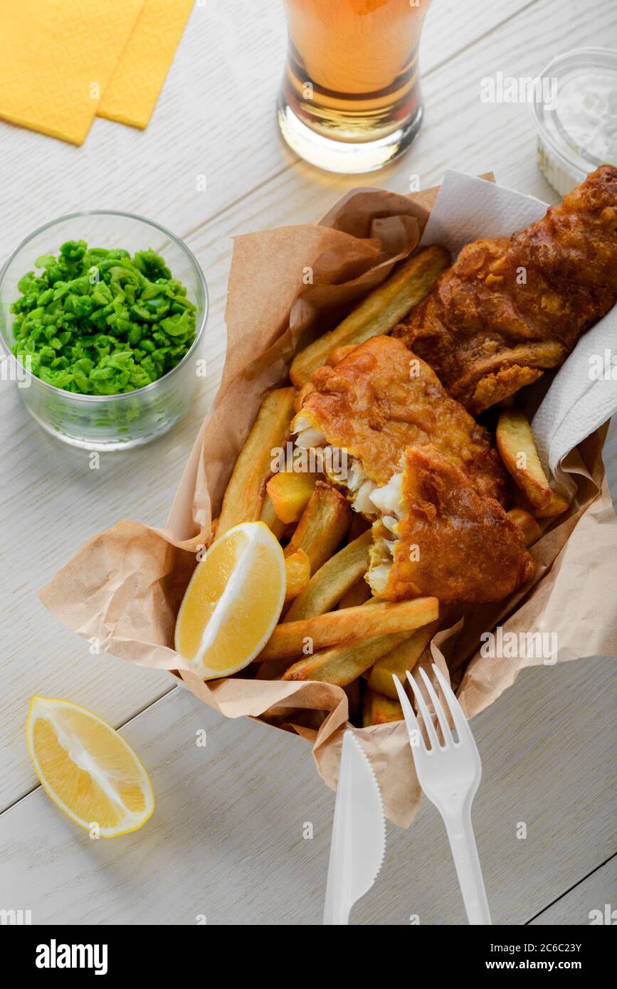 Pesce e patatine avvolti in carta. Purè di piselli verdi e fette di limone Foto Stock