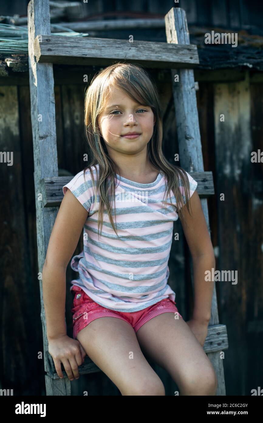 Ritratto di una bambina seduta su una scala in legno nel villaggio. Foto Stock