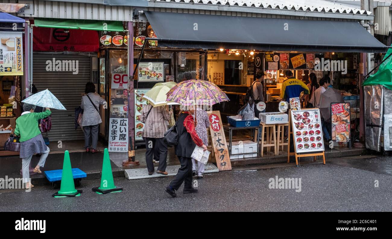 Folla di persone che passeggiano per la piccola e stretta strada del mercato esterno di Tsukiji durante una giornata piovosa, Tokyo, Giappone Foto Stock