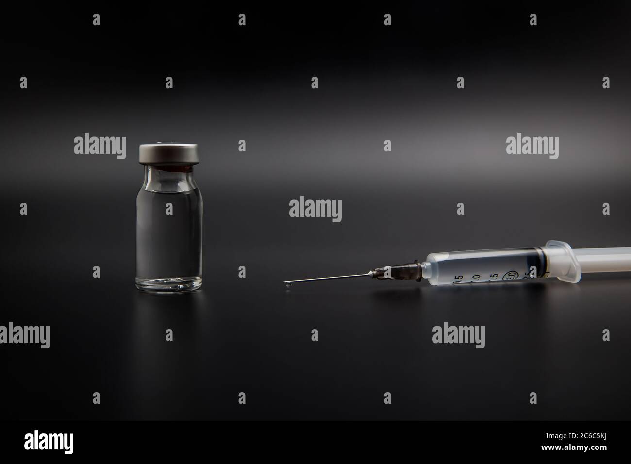 Flacone di vaccino piccolo (flaconcino) e siringa medica con una goccia di vaccino sull'ago, isolato su fondo nero per la vaccinazione di preventio Foto Stock