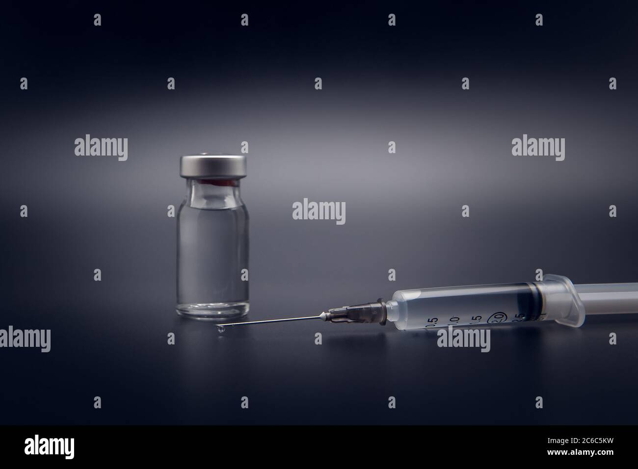 Flacone di vaccino piccolo (flaconcino) e siringa medica con una goccia di vaccino sull'ago, isolato su fondo nero per la vaccinazione di preventio Foto Stock