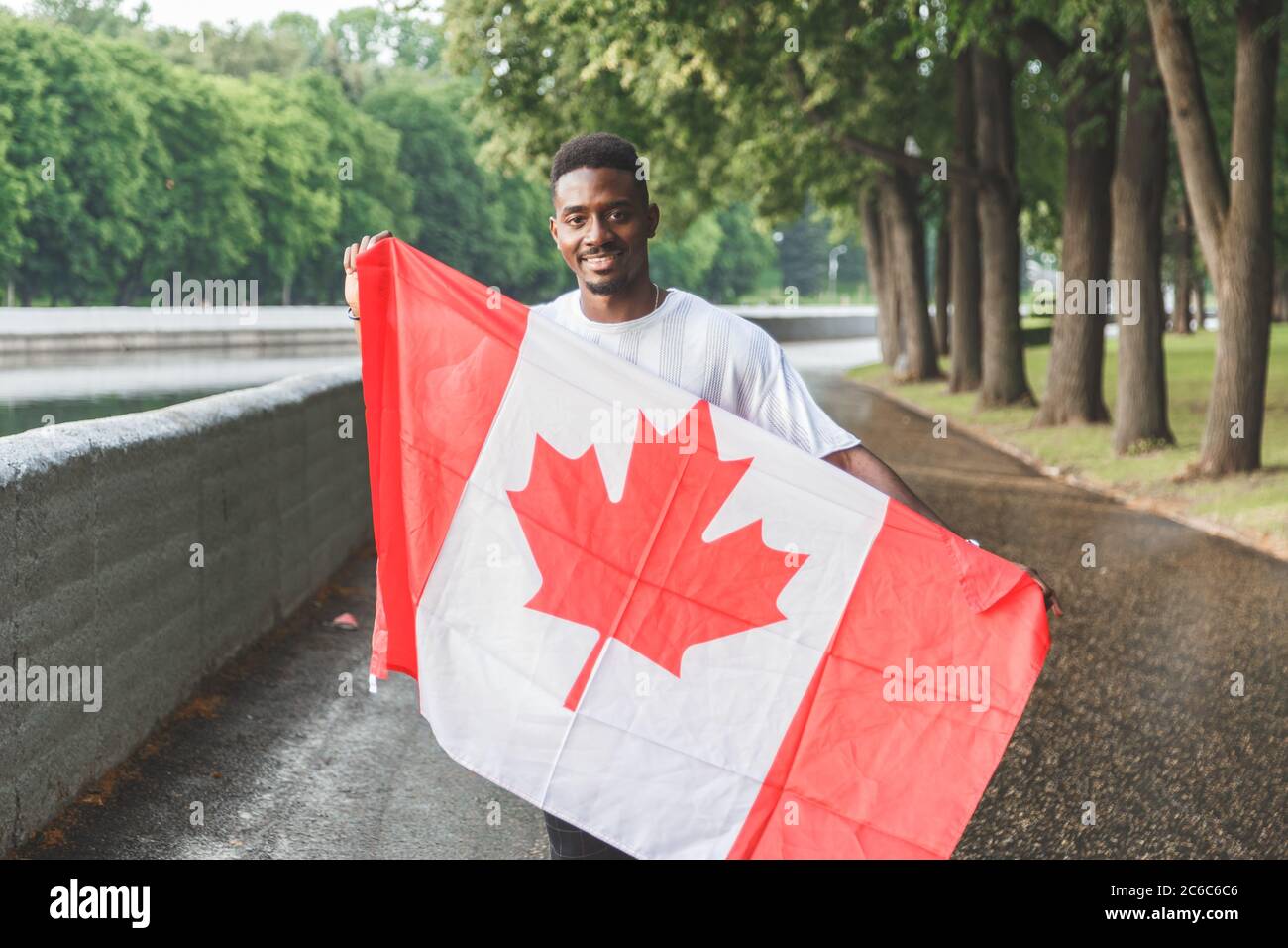 Bell'uomo afro-americano con bandiera canadese sorridente alla macchina fotografica, in piedi all'aperto. Foto Stock