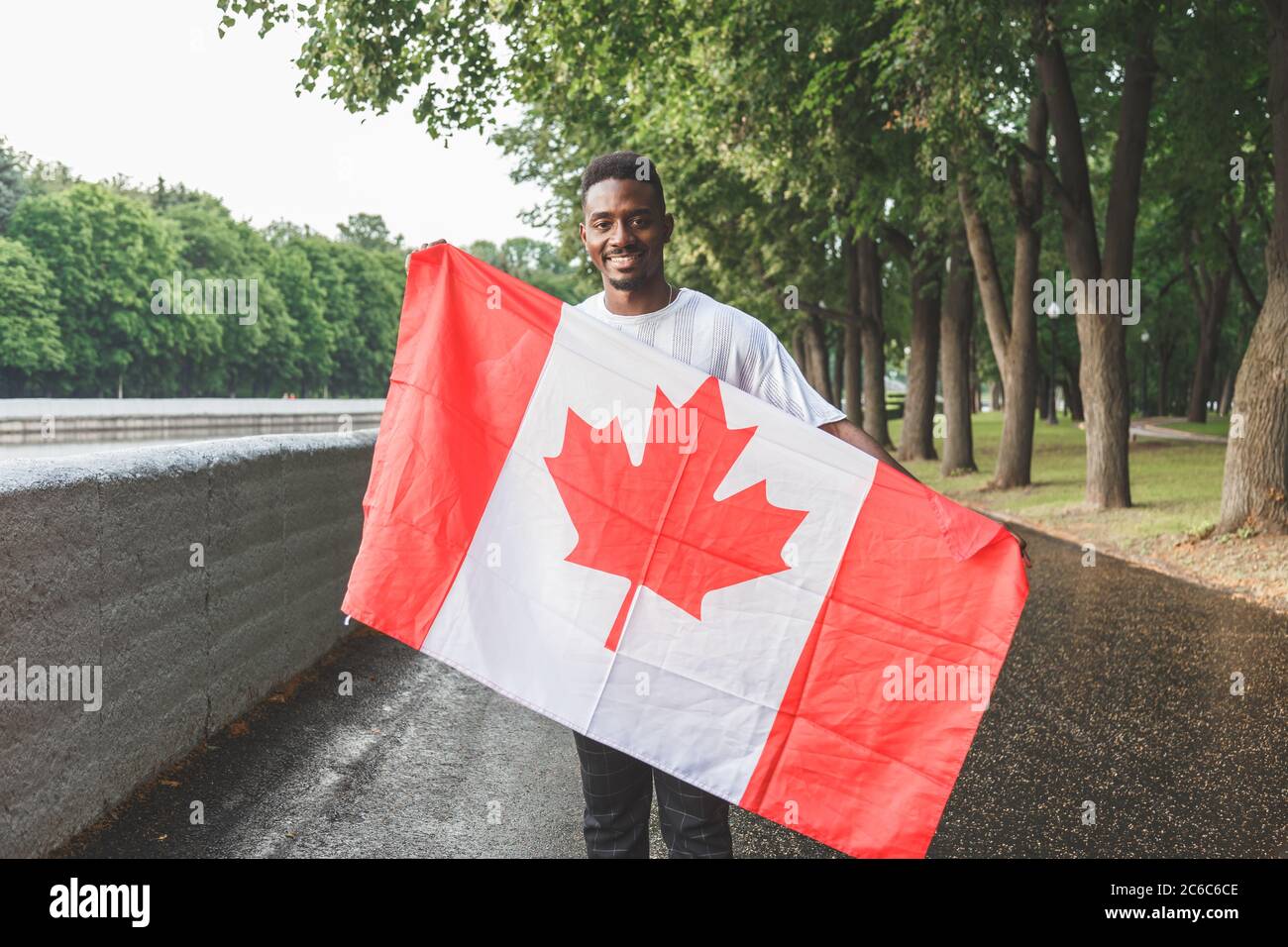 Bell'uomo afro-americano con bandiera canadese sorridente alla macchina fotografica, in piedi all'aperto. Foto Stock