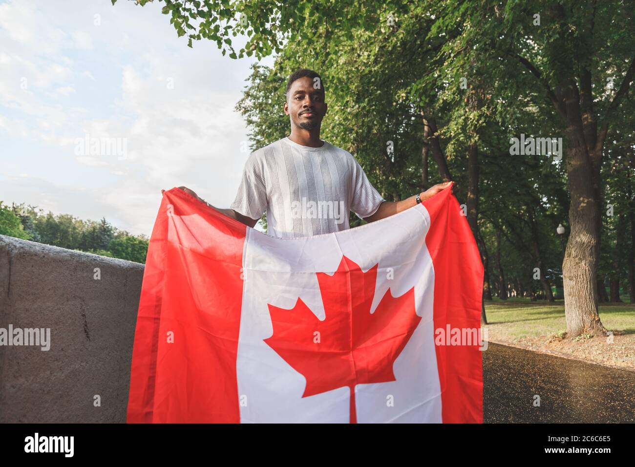 Bell'uomo afro-americano con bandiera canadese seriamente guardando la macchina fotografica, in piedi all'aperto. Foto Stock