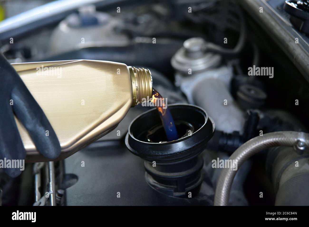 Aggiunta di olio a un'auto. Mano dell'uomo che tiene una ciotola di olio motore e versato nel motore. Da barattoli di olio che versano nel motore dell'automobile. Foto Stock