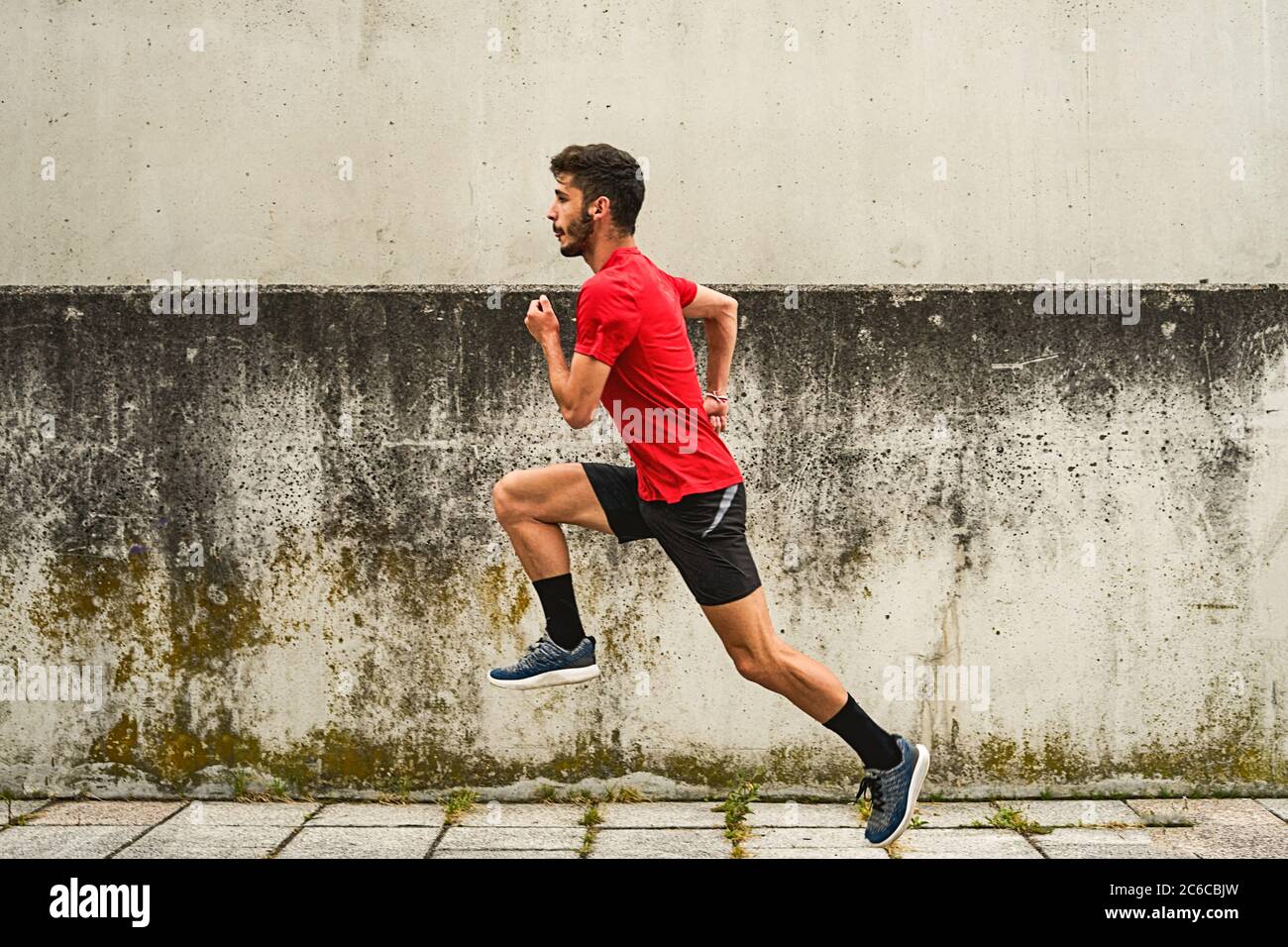 giovane uomo che corre in una camicia rossa e pantaloni neri attraverso il parco Foto Stock