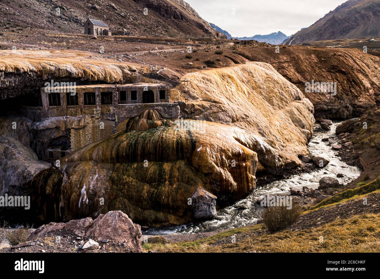 Vista panoramica del torrente che passa sotto le terme sul ponte Inca con una cappella e le montagne marroni sullo sfondo di una nuvola Foto Stock