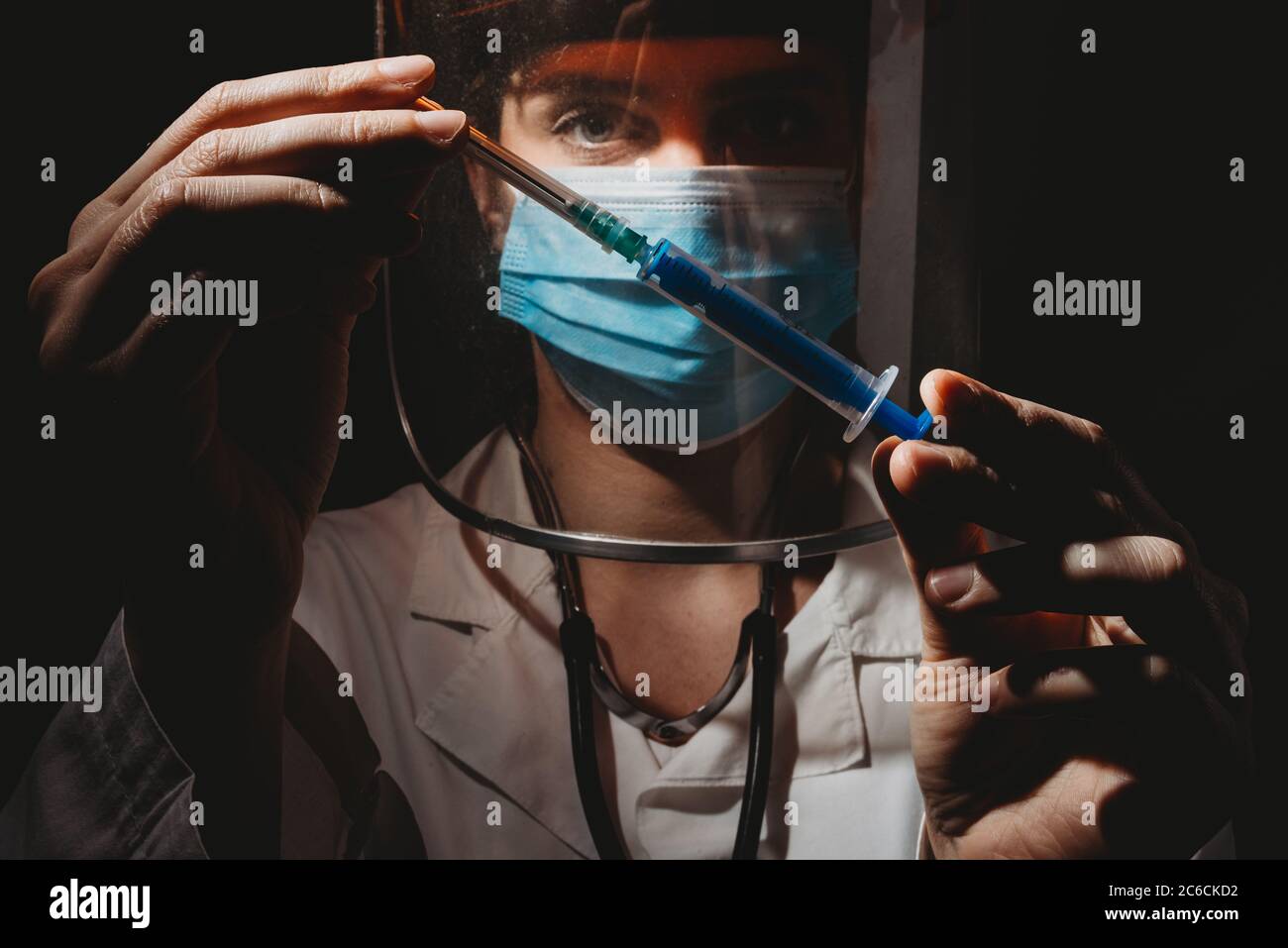 medico femminile con maschera e scudo che tiene in mano il vaccino su sfondo nero Foto Stock