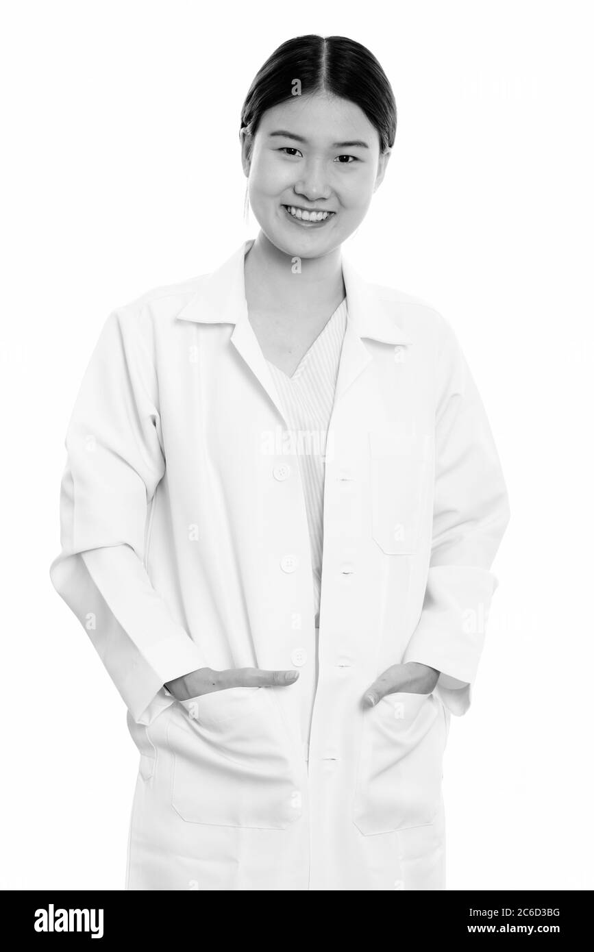 Studio di giovane donna asiatica felice medico sorridente con le mani sulle tasche Foto Stock