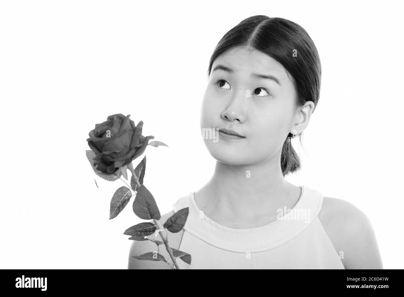 Studio di giovane bella donna asiatica che tiene rosa rossa mentre pensa Foto Stock