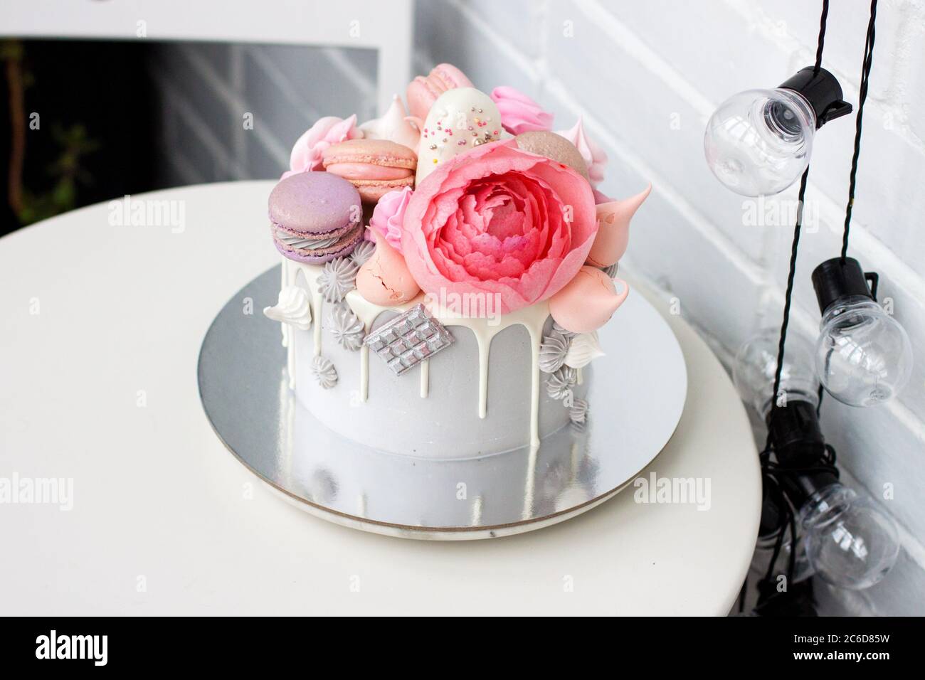 Torta grigia moderna con fiori di pony rosa, cioccolato e macaroon per un matrimonio o una celebrazione. Sfondo bianco. Foto Stock