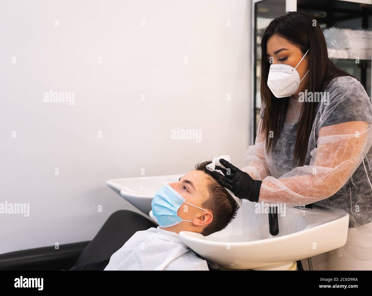 Giovane uomo con una maschera protettiva appoggiata su un luccio mentre la testa viene asciugata con un asciugamano in un parrucchiere Foto Stock