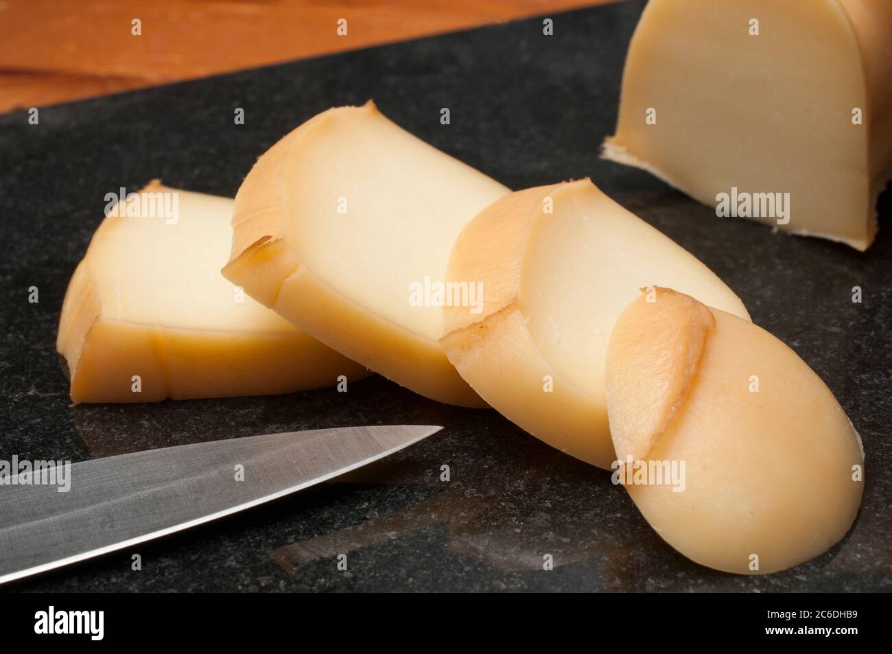 Fette di scamorza affumicata, tipico formaggio italiano su un tagliere di granito nero poggiato su un tavolo di legno Foto Stock