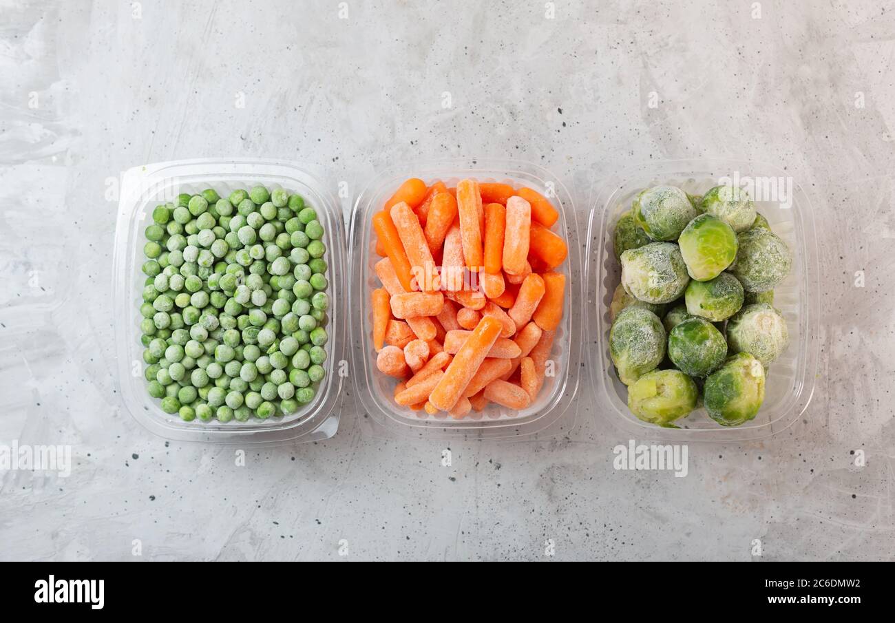 Verdure surgelate come piselli verdi, germogli di bruxelles e carote per bambini nelle scatole di stoccaggio su fondo grigio cemento, vista dall'alto, piatto Foto Stock