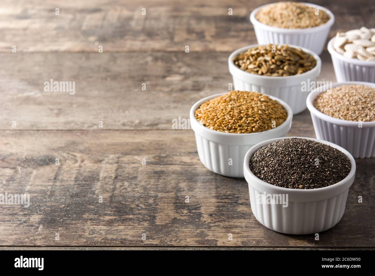 Assortimento di semi diversi in ciotola su tavolo di legno. Zucca, lino, cia, girasole e semi di sesamo. Foto Stock